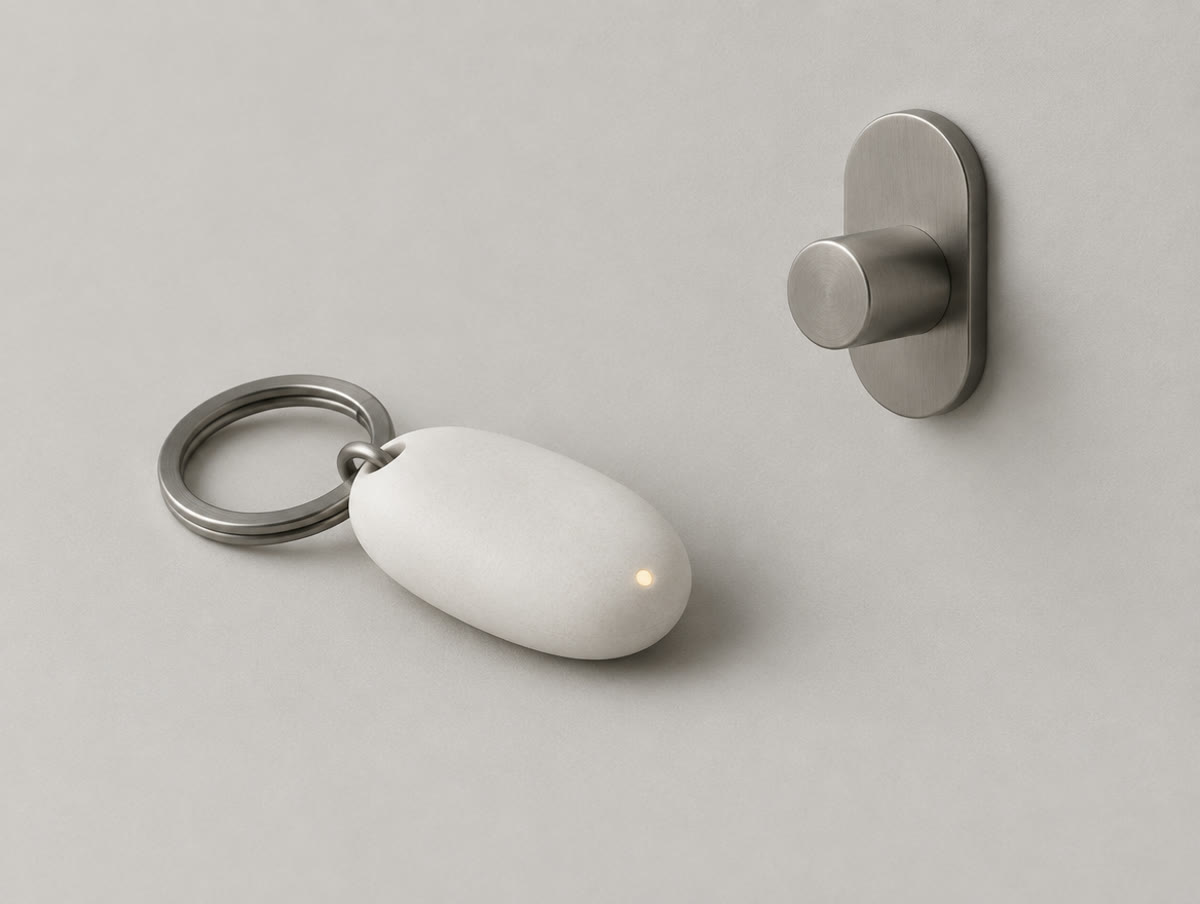 Pebble-shaped chalk-white household key on a titanium ring, beside its wall hook.